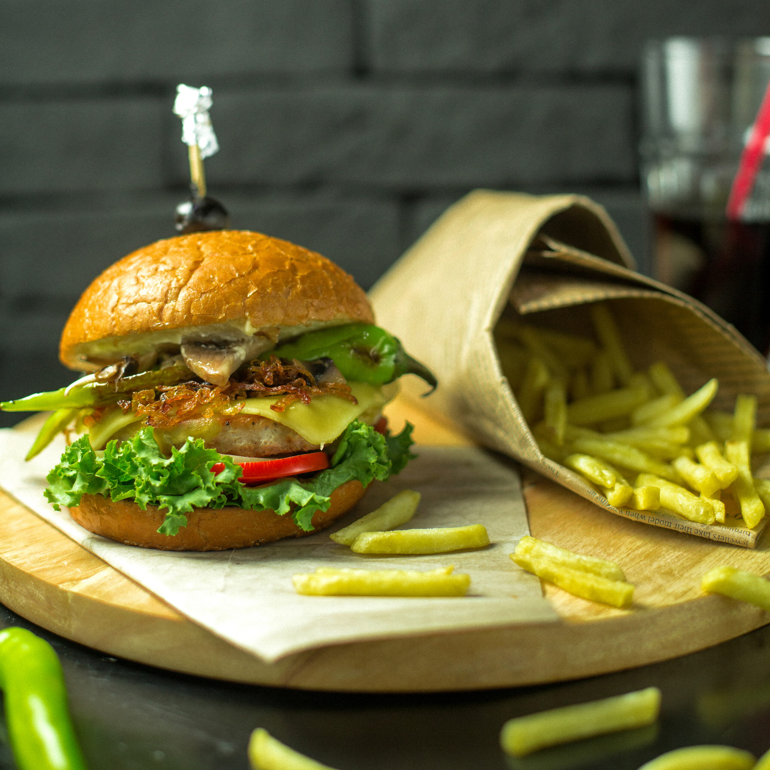 side view of chicken burger with melted cheese tomatoes and lettuce served with french fries on a wooden board